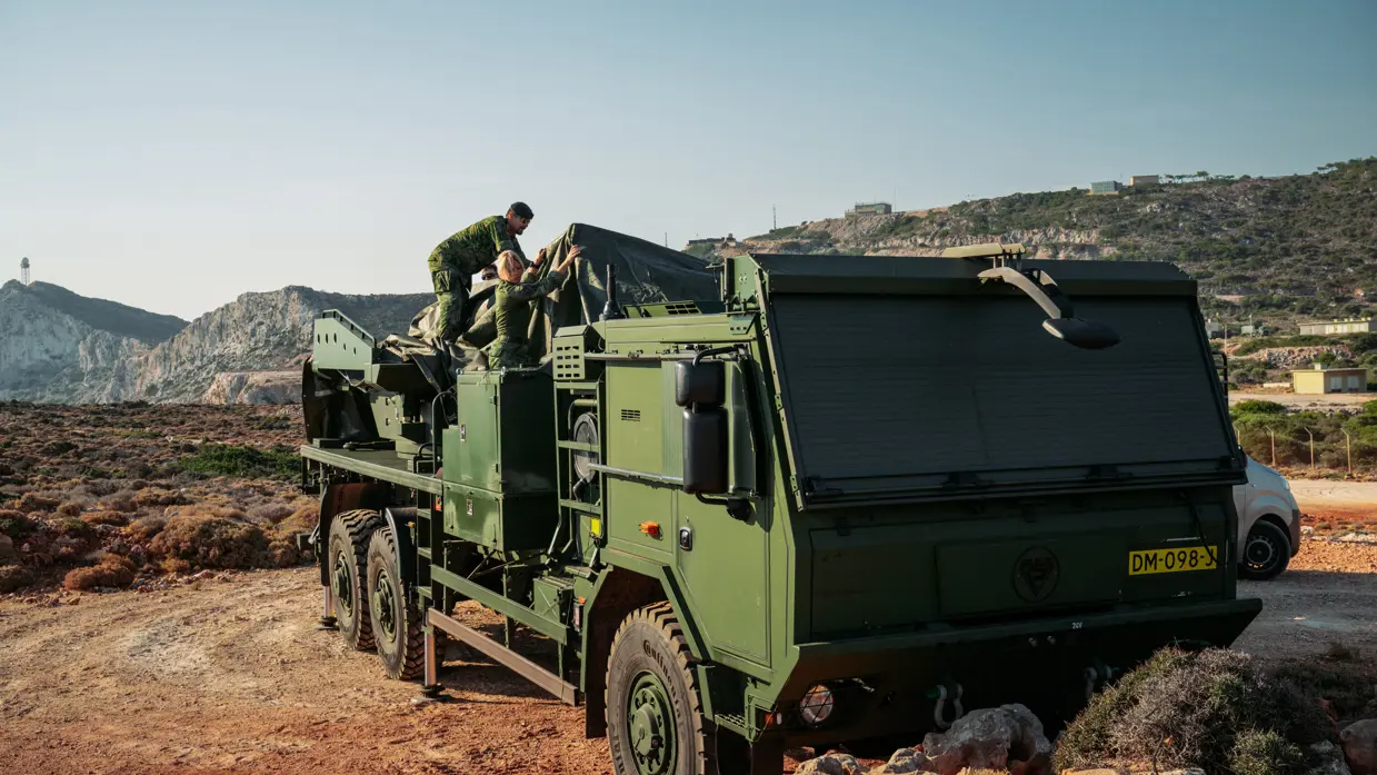Een militair is bezig met de techniek bovenop de wagen met een wapensysteem.