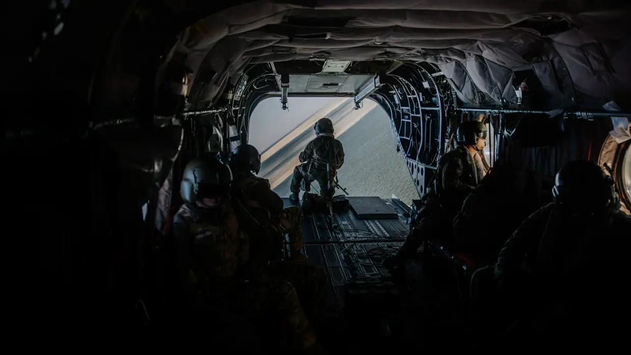 Een groep militairen is zichtbaar in de vrachtruimte van een Chinook, met uitzicht op de grond beneden.