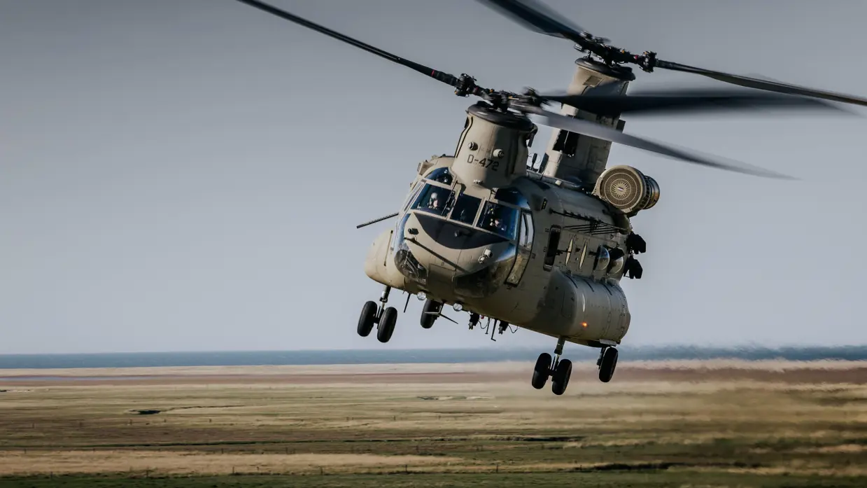 Een Chinook-helikopter vliegt door de lucht, met erachter de horizon zichtbaar.