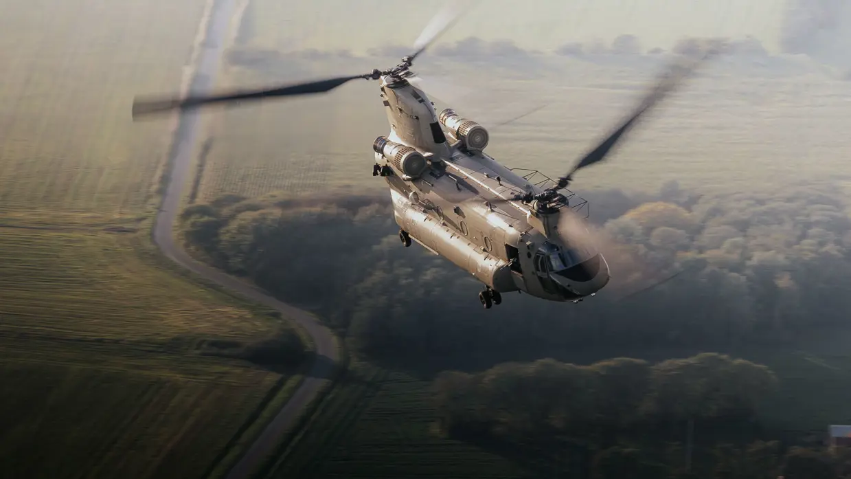 Een Chinook-helikopter vliegt boven een landschap.