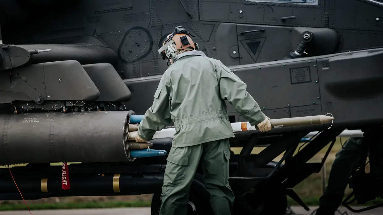Een militair laadt een raket in het wapensysteem van een Apache-helikopter.