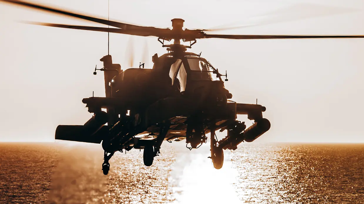 Een vliegende Apache-helikopter van achter fel verlicht wordt de reflectie van de ondergaande zon op het water.
