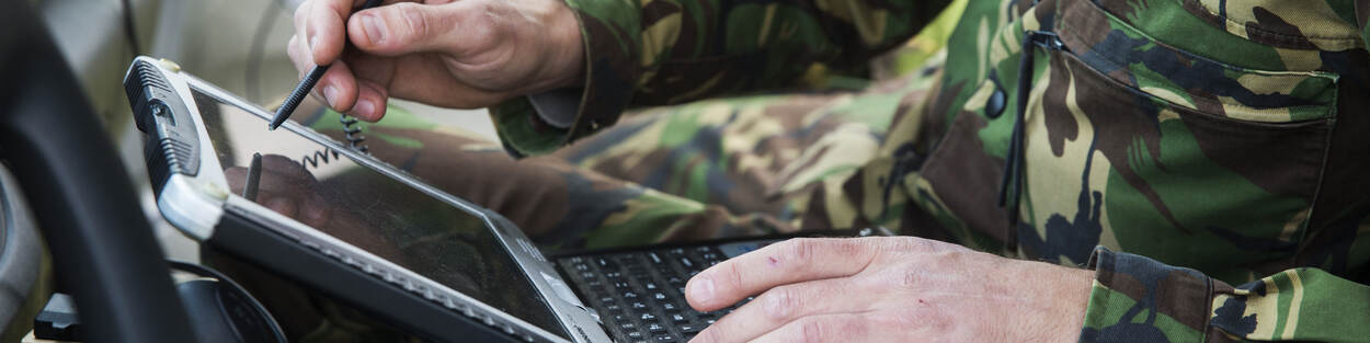 Een militair wijst met een pen op beeldscherm van laptop.