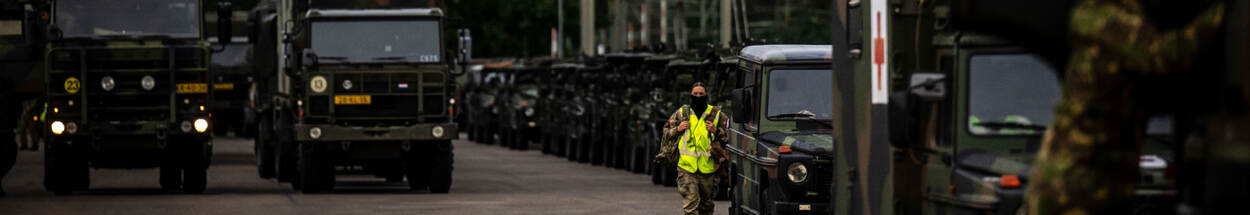 Persoon in een geel hesje loopt tussen de militaire voertuigen.