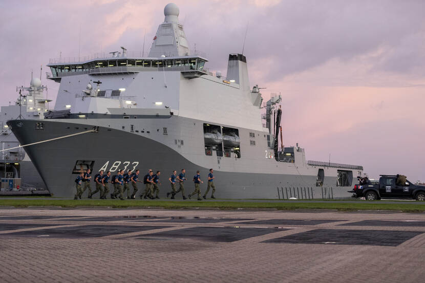 Rennende mariniers in de marinehaven, achter hen marinefregat A833.