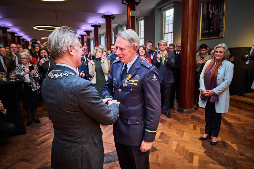 Commodore-vlieger prof.dr. Frans Osinga ontvangt de koninklijke onderscheiding. Familie en genodigden op de achtergrond.