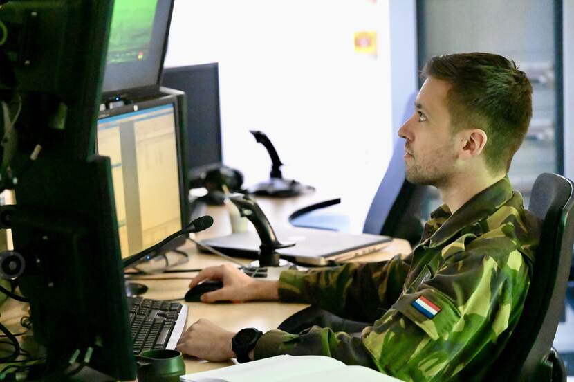 Een militair aan zijn bureau kijkt op beeldschermen.