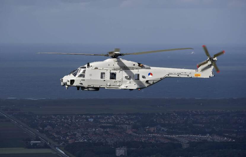 Een NH90-maritieme gevechtshelikopter vliegt boven een kustgebied.
