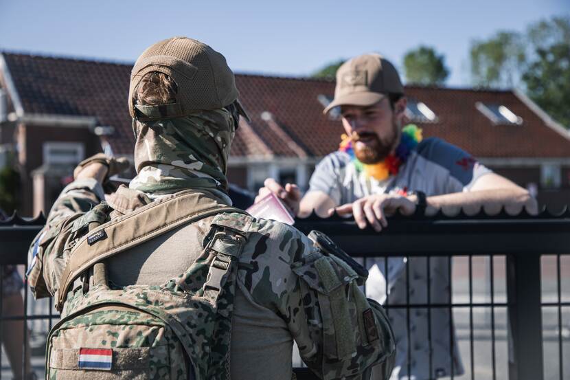 Militair op rug praat met burger achter een hek.