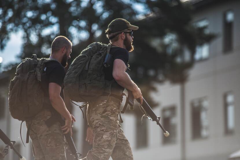 2  militairen met geweer en bepakking op hun rug.