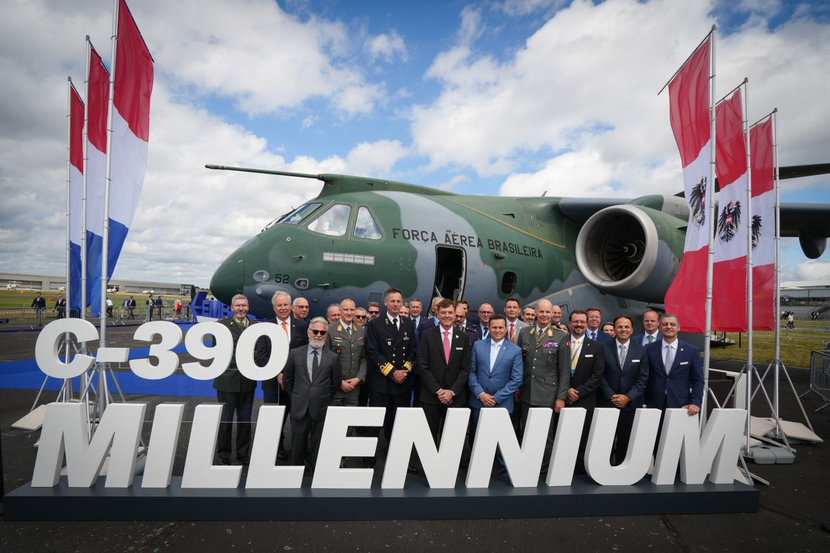 Een groep mensen poseert op de stand van Embrear tijdens de Farnborough Airshow.