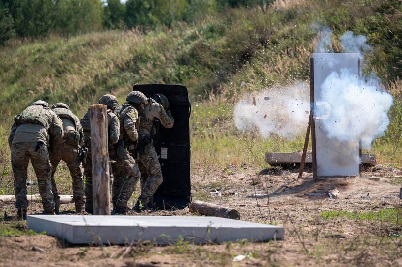 Ontploffing van deur. Groepje militairen zoeken op afstand bescherming.