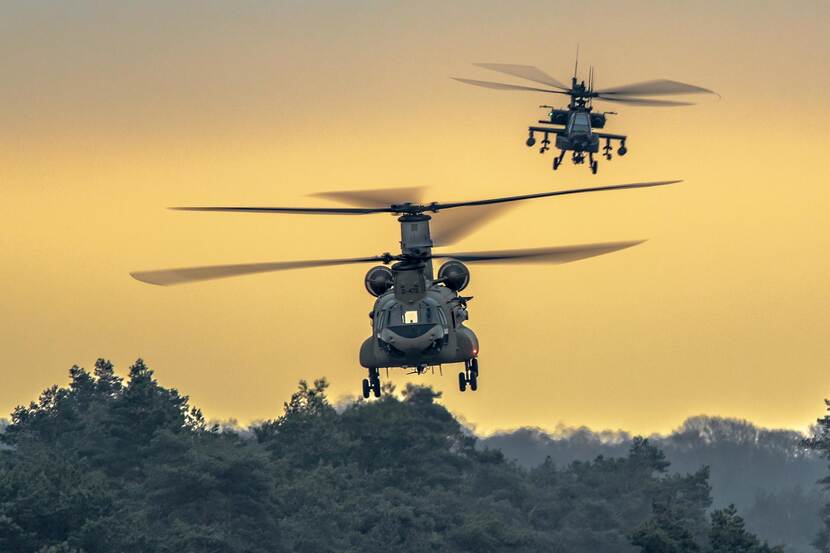 Een Chinook-transporthelikopter gevolgd door een Apache-gevechtshelikopter.