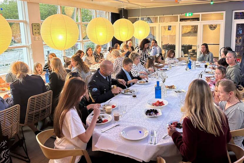 Overzicht van lange tafels waaraan vrouwen en kinderen zitten te eten.