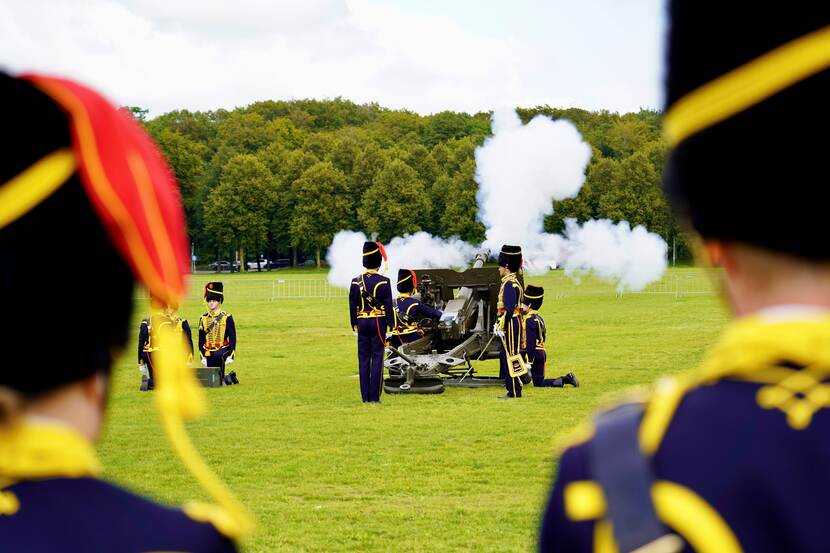 Kanon met rookwolk. Militairen in ceremonieel tenue (Gele Rijders) staan ernaast.