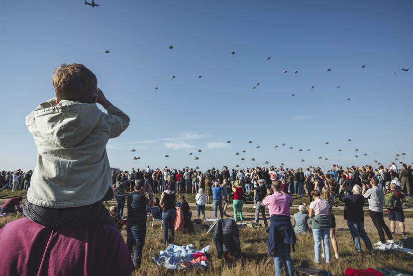 Publiek ziet parachutisten landen op heide.