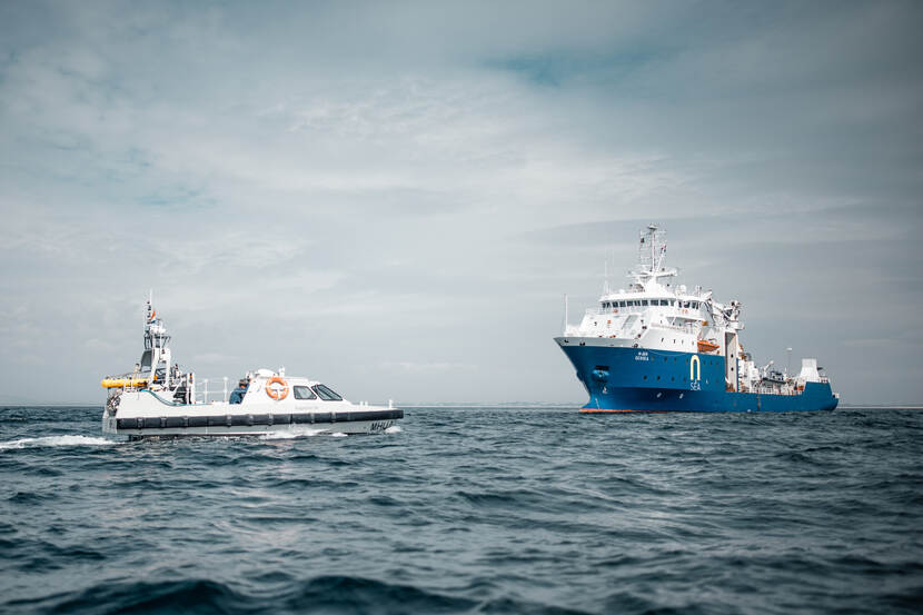 Een schip van de marine en een varende drone op het water.