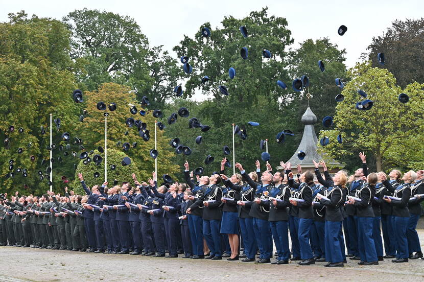 Geslaagde officieren gooien hun pet en baret in de lucht.