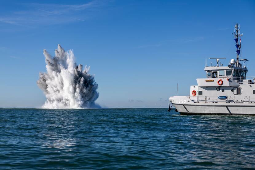 Ontploffing in zee. Marinevaartuig vaart op afstand.