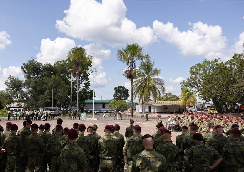 Een groep militairen van de achterkant gezien. Staand in een halve cirkel tijdens de openingsceremonie van de jungletraining.