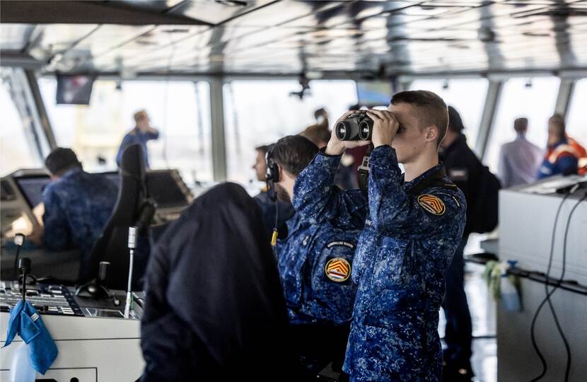 Een marineman kijkt op de brug van het schip door een verrekijker.