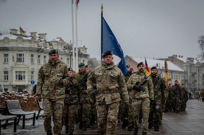 Militairen van de eFP lopen in parade door stad. Met NAVO-vlag.