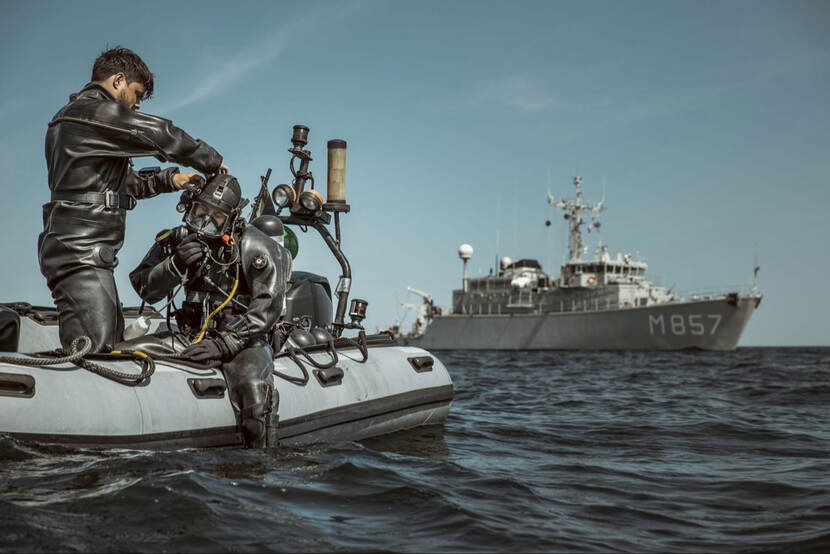 Een duiker en een waterscooter op zee, met daarachter Zr.Ms. Makkum