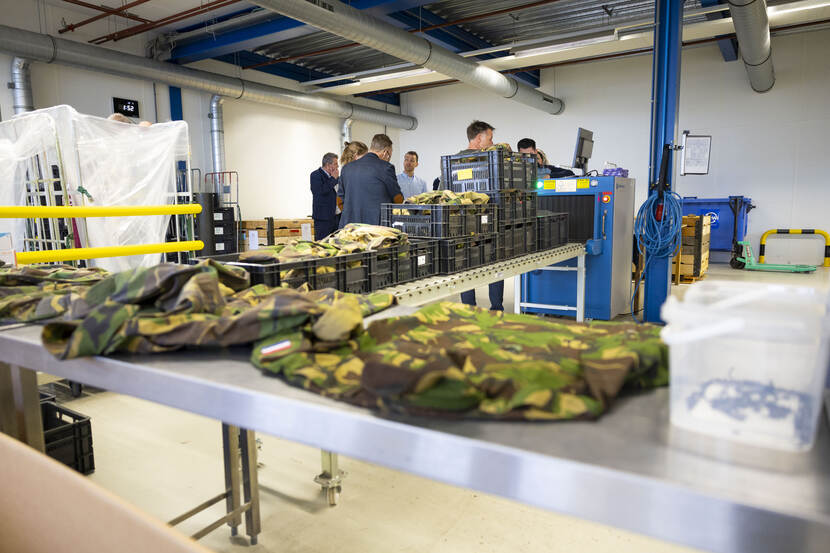 Militaire tenues op een glimmende tafel, met mensen op de achtergrond.