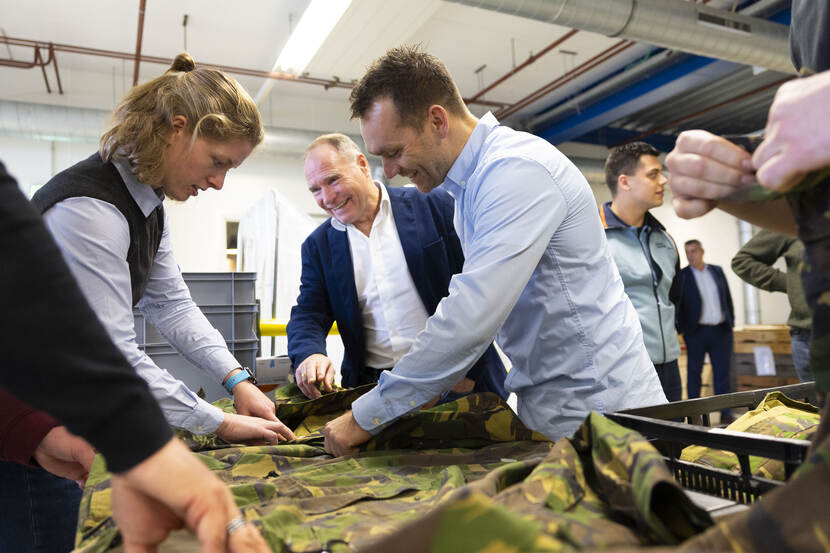 Medewerkers van het DJI raken de militaire uniformen aan, die op een glimmende tafel liggen