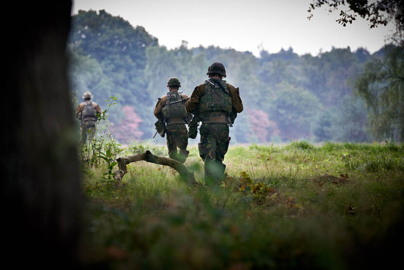 Militairen, vanaf de rug bezien, lopen door het beboste militaire oefenterrein De Vlasakkers.