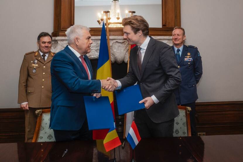 Minister Brekelmans (rechts) schudt voor grote schouw met spiegel de hand Roemeense collega.