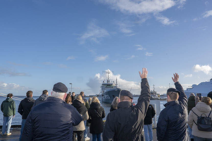 Mensen zwaaien vanaf de kade een marineschip uit.