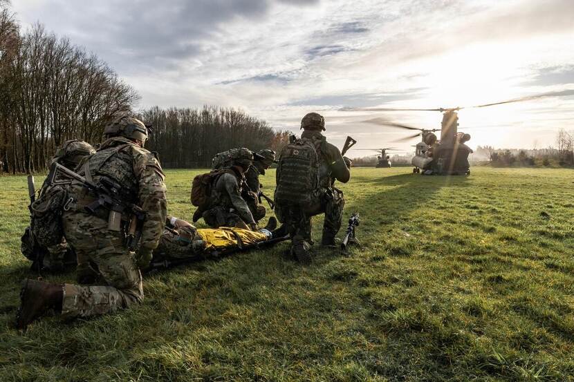 Militairen op een veld. In de verte een Chinook-transporthelikopter.