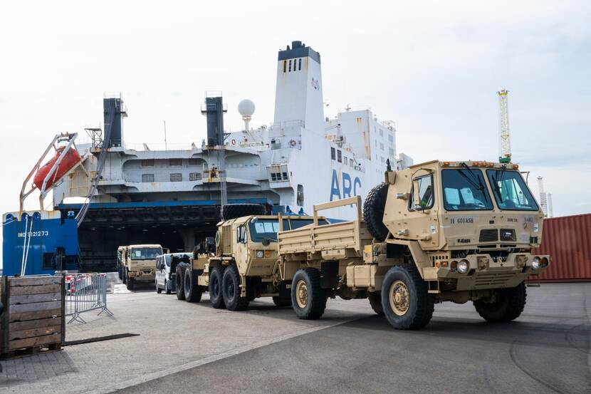 Militaire vrachtwagens komen rijdend uit de laadruimte van een schip.