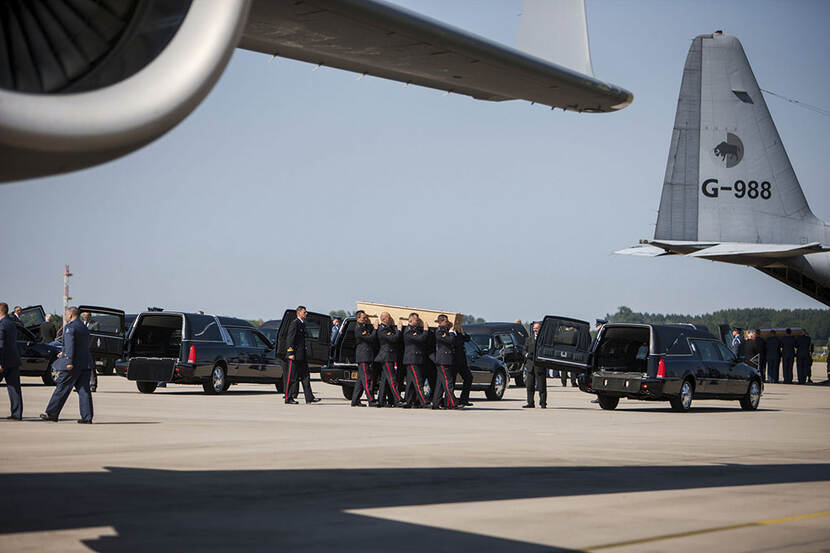 Militaire dragers dragen een kist met stoffelijk overschot van een vliegtuig in een rouwwagen.