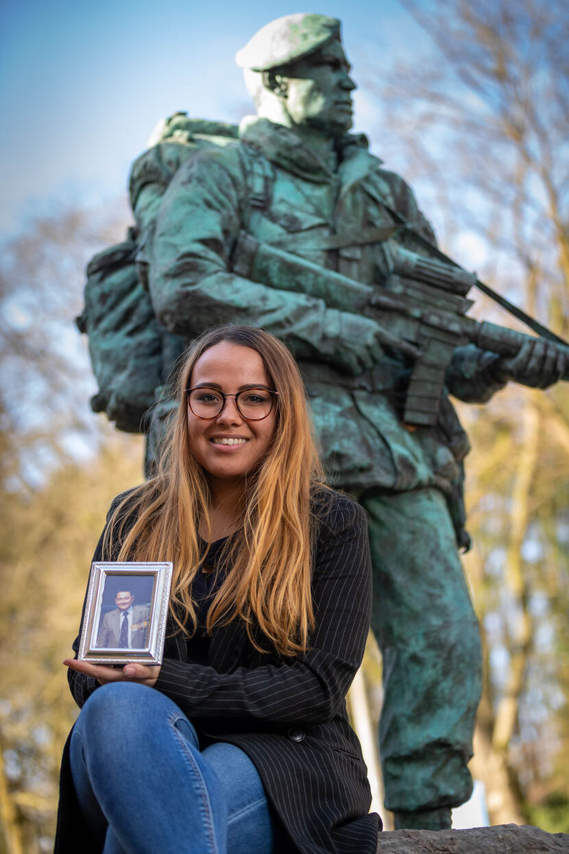 Vrouw zittend met een foto in de hand voor een bronzen beeld.