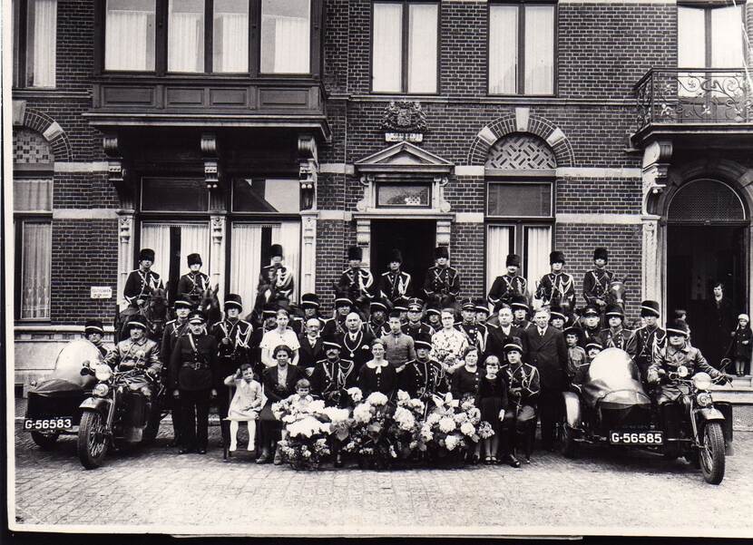 Zwart-witgroepsfoto voor gebouw Koninklijke Marechaussee, inclusief paarden en zijspanmotoren.