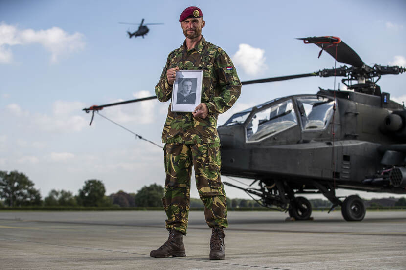 Militair Boomstra poseert met foto van opa voor Apache-gevechtshelikopter. Op achtergrond vliegt Cougar-transporthelikopter.