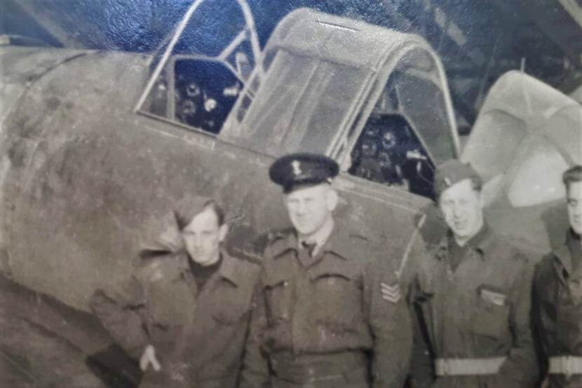 4 militairen op een zwart-wit foto poseren voor een oud vliegtuig.