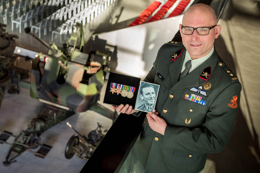 Ted Jansen met op achtergrond bij wapensysteem van vroeger. Toont foto en onderscheidingen van zijn opa.