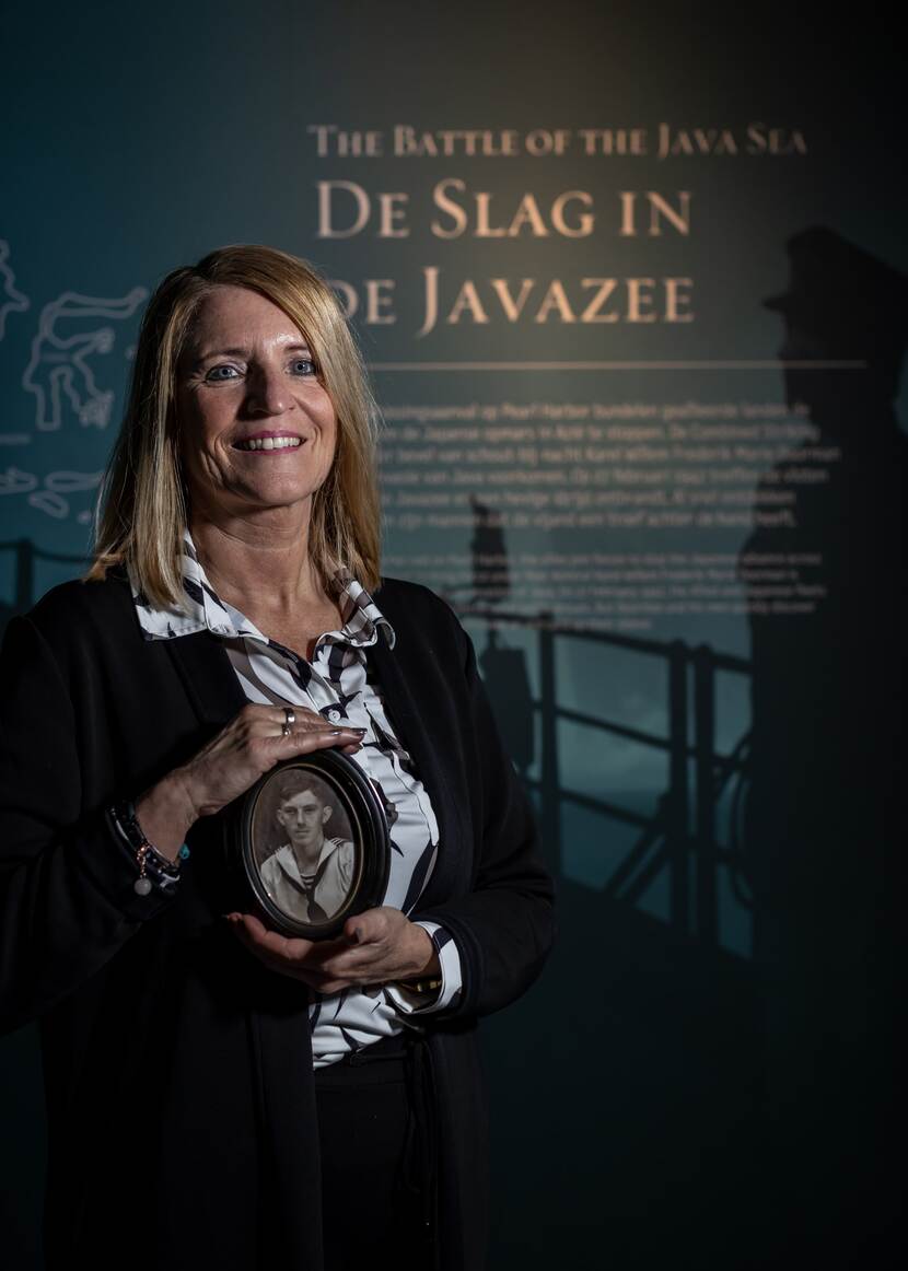Vrouw met historische foto in de hand voor informatiebord 'Slag in de Javazee' bij Marinemuseum.