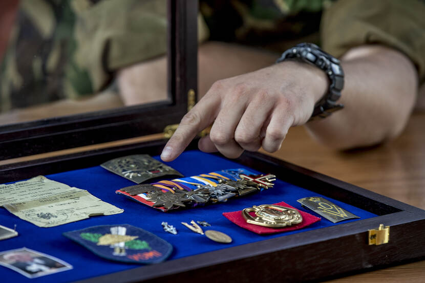 Een hand wijst naar militaire onderscheidingen in een koffer.
