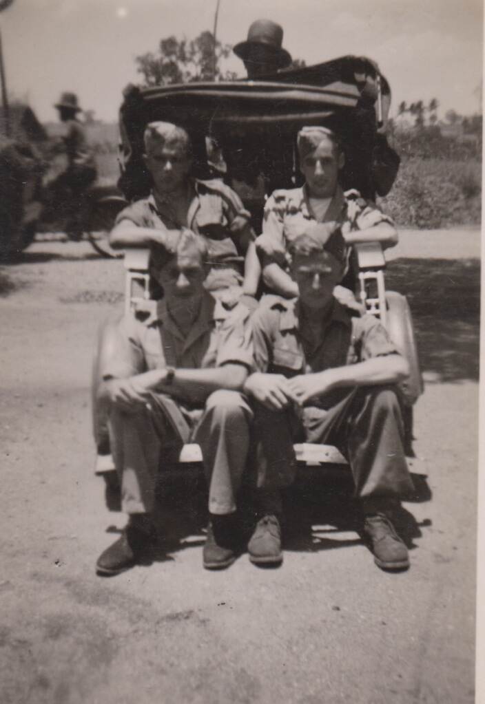 Oude foto met 4 militairen zittend op de achterkant van een auto.