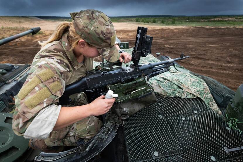 Vrouwelijke militair in een tank controleert geweer.