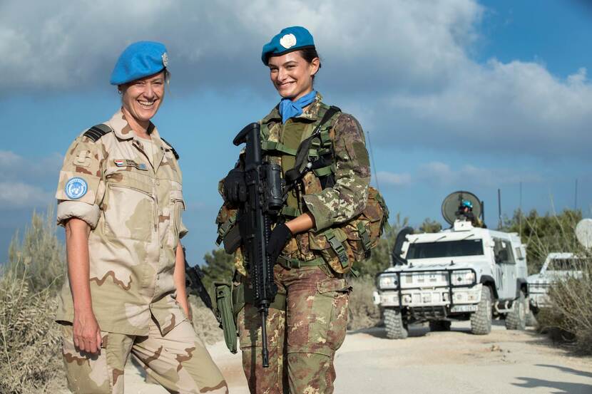 2 vrouwelijke militairen op een zandweg. Eén van hen draagt een geweer.